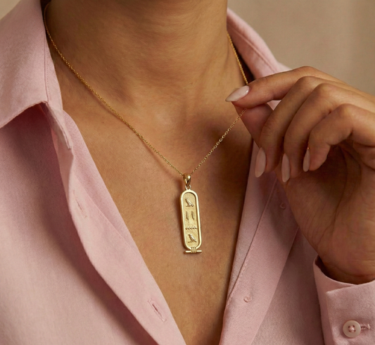 Gold necklace with a pendant worn by a person in a pink shirt.