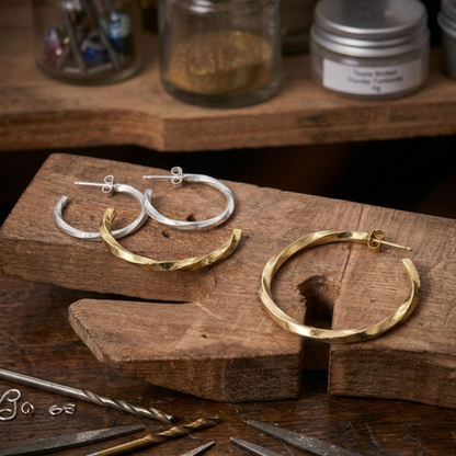 Gold and silver hoop earrings on a wooden block with jewelry-making tools in the background.