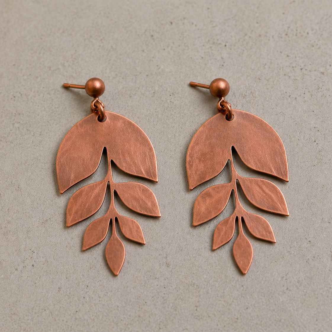 Copper leaf-shaped earrings on a gray background
