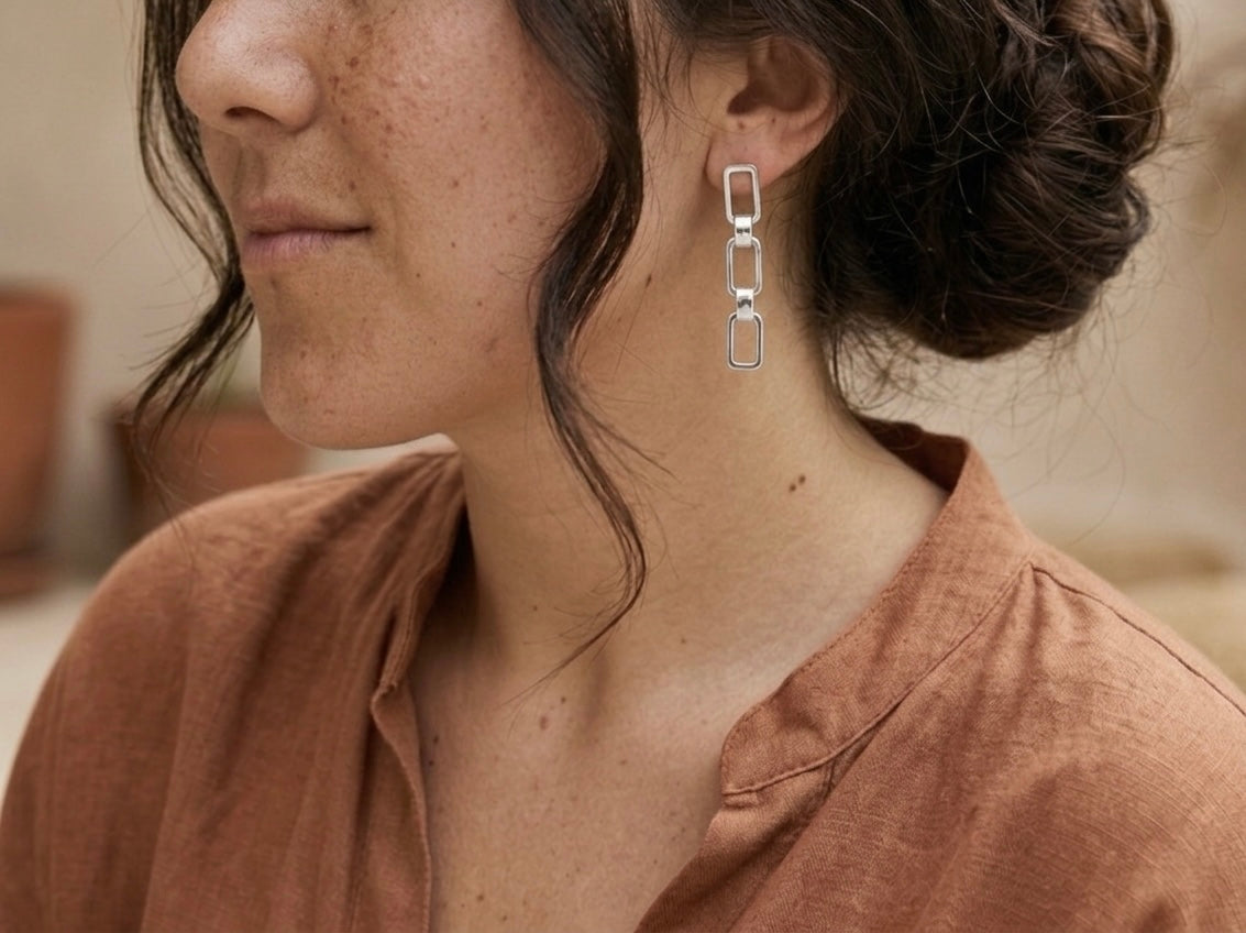 Close-up of a person wearing silver chain earrings with a blurred background