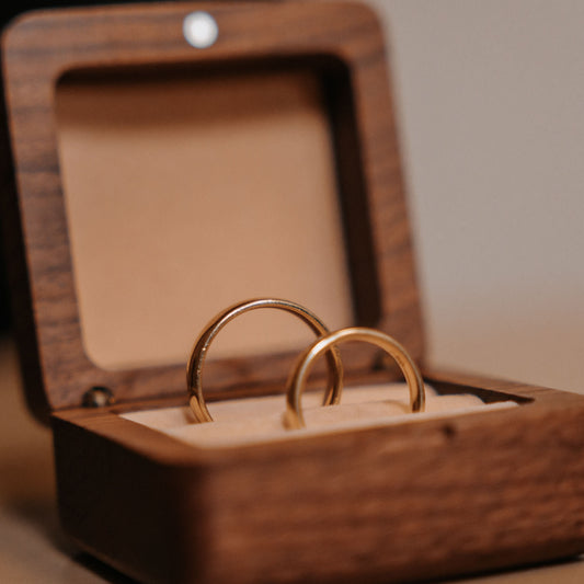 Two gold rings in a wooden box on a neutral background